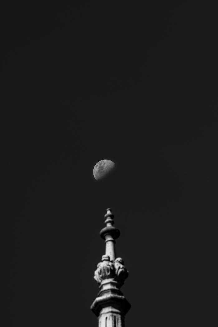 Monochrome photograph featuring a detailed architectural spire with the moon in the background.